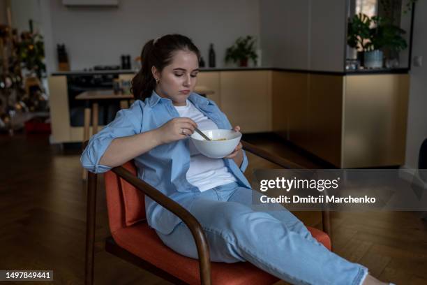 unhappy overweight young woman sitting on chair with bowl of cereals, feeling unmotivated to diet - fat loss stock pictures, royalty-free photos & images