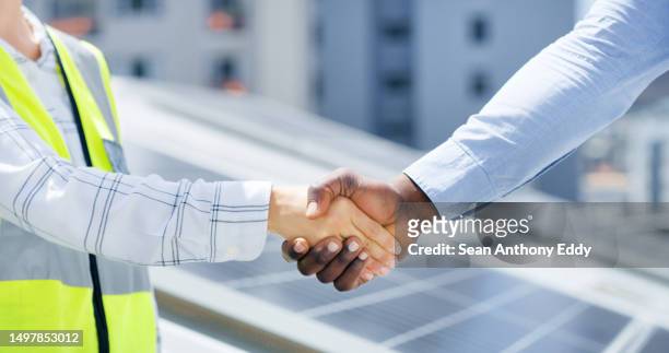 closeup of hands of man and woman greeting with a handshake while installing a solar panel. two diverse colleagues shaking hands for construction and building deal - generation contract stock pictures, royalty-free photos & images