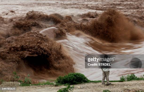 An Indian villager watches fast moving water during a flash flood of the Tawi river on the outskirts of Jammu on August 4, 2012. Some 27 people,...