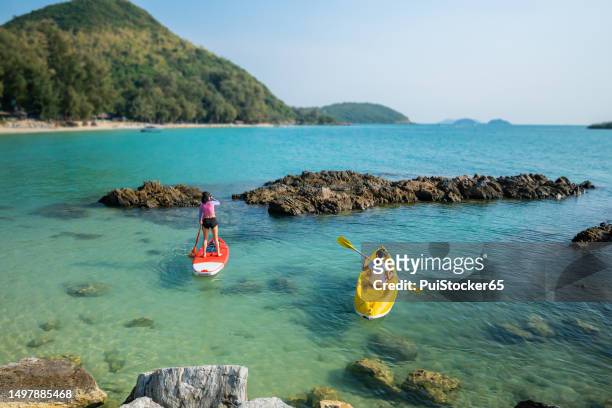 asian athletic woman on paddle board with friend on kayak at the sea. outdoor water sport and travel on summer holiday thailand. - strand pattaya stockfoto's en -beelden