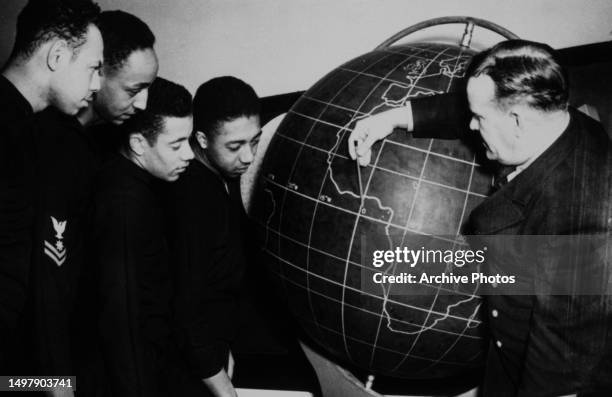 Students listen to a teacher pointing to a marking on a globe during a US Navy navigation class, circa 1940.