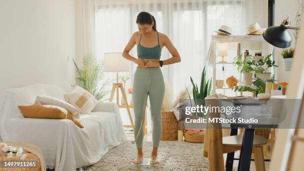 young asian athletic woman with a tape measure body perfect slim weight loss on scales in living room at home. diet and healthy weight loss. - woman measuring tape stock pictures, royalty-free photos & images