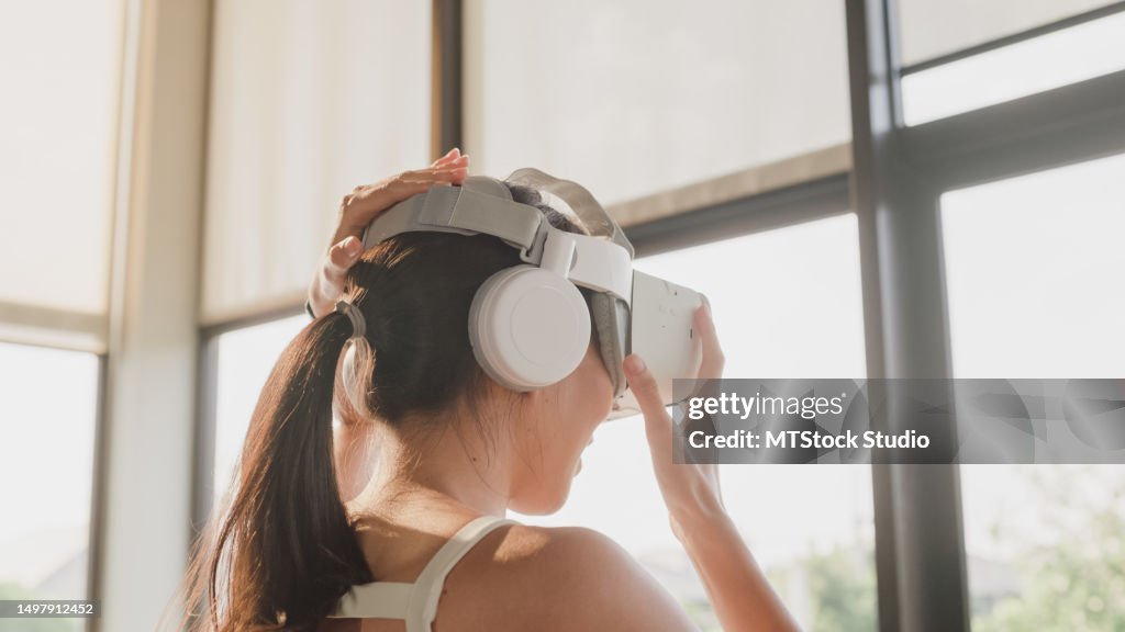 Junge asiatische athletische Sportlerin, die eine VR-Brille trägt und auf Laufbändern läuft und aktiv im modernen Fitnessstudio trainiert. Sportler trainieren.