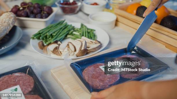 nahaufnahme junger asiatischer freundinnen hält messerschneiden pflanzliche mahlzeit auf holzbrett auf küchentisch zu hause in der nacht. lebensstil gesundes essen essen genießen natürliches leben. - fleischersatz stock-fotos und bilder