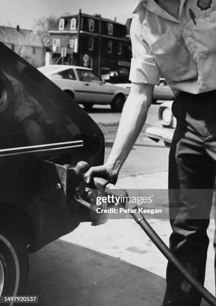 Shell gas station attendant, his sleeves rolled up, holds a fuel pump at the open cap of a car's fuel tank at a gas station in New York City, New...