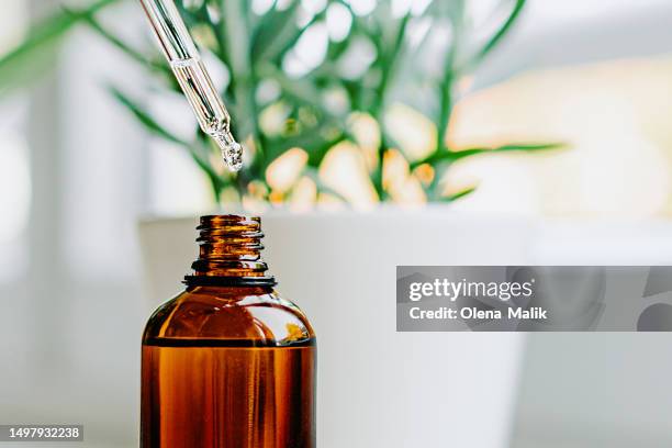 close up of face serum pouring from a pipette into an amber glass bottle. natural skincare and essential oil aromatherapy. health and wellness concept. copy space. - etherische olie stockfoto's en -beelden