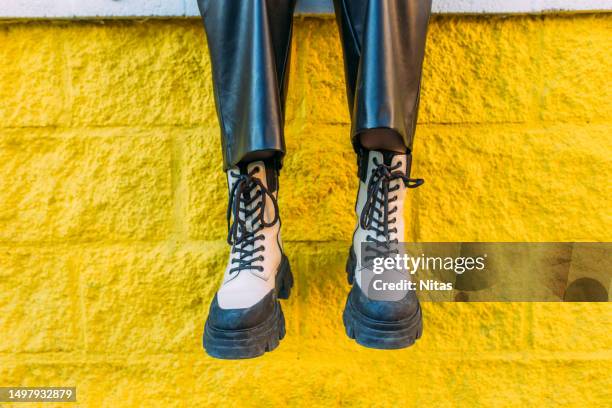black and white fashionable boots on a yellow wall - botas-blancas fotografías e imágenes de stock