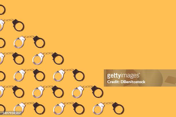 pattern of metal locked handcuffs, on the left side, on a yellow background. police, prison, jail, prisoner, illegal, robbery, law, trial and thief concept. - agent cash stockfoto's en -beelden