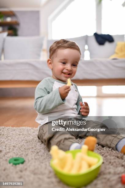 smiling baby relaxing with toys and snacks on the floor - baby eating imagens e fotografias de stock