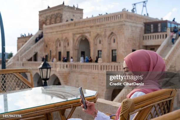 a woman with a headscarf sitting in the view of the stone mansion in midyat district of mardin province. - vintage embellishment stock pictures, royalty-free photos & images