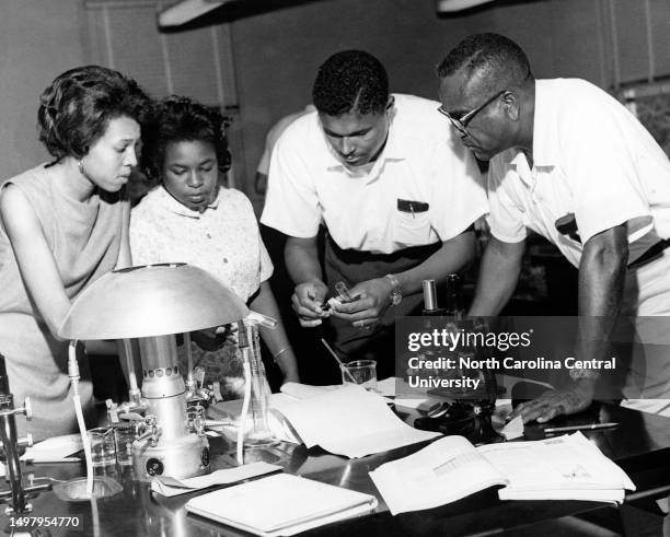 Faculty members and university students setting up fractional distillation apparatus while performing experiment in college laboratory.