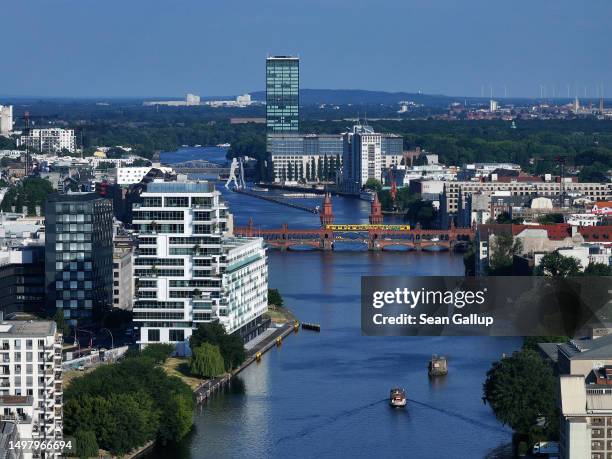 In this aerial view a yellow U-Bahn underground train passes over Oberbaumbruecke bridge and the Spree River as the Molecule Man sculpture stands...