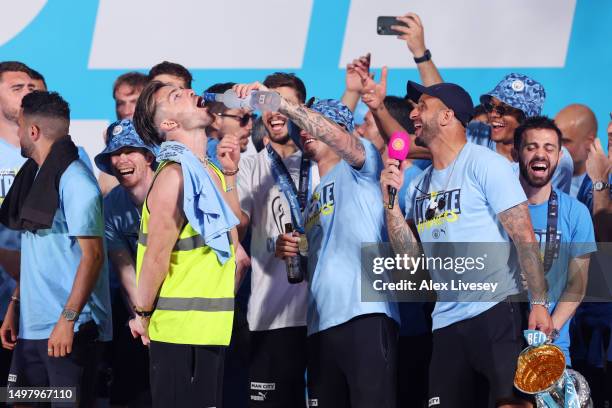 Kalvin Phillips of Manchester City pours Grey Goose into the mouth of Jack Grealish as Kyle Walker looks on as they celebrate on stage in St Peter's...