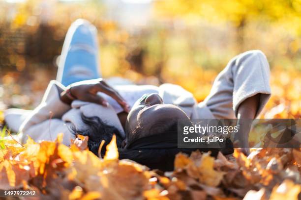 young adult black woman lying down in autumn leaves and relaxing - october 22 stock pictures, royalty-free photos & images