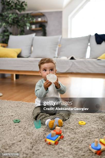 neonato che si siede sul pavimento e acqua potabile - baby eating toy foto e immagini stock