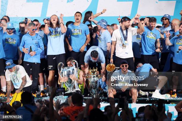 Players of Manchester City celebrate on stage in St Peter's Square as Jack Grealish embraces the UEFA Champions League Trophy, Aymeric Laporte lifts...