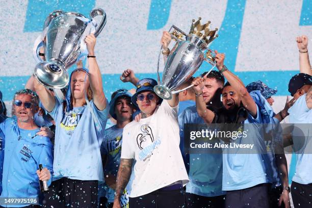 Erling Haaland lifts the UEFA Champions League Trophy as Ederson and Riyad Mahrez lift the Premier League Trophy on stage in St Peter's Square during...