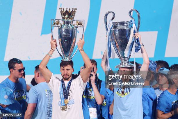 Ruben Dias of Manchester City celebrates with the Premier League Trophy as Kevin De Bruyne celebrates with the UEFA Champions League Trophy on stage...