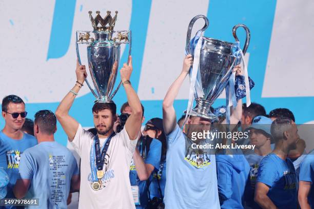 Ruben Dias of Manchester City celebrates with the Premier League Trophy as Kevin De Bruyne celebrates with the UEFA Champions League Trophy in St...