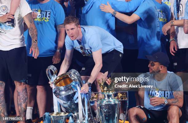 Kevin De Bruyne of Manchester City celebrates with the UEFA Champions League Trophy, FA Cup Trophy as Kyle Walker celebrates with the Premier League...