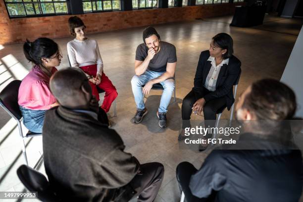 mid adult man talking during a therapy group - reünie sociaal stockfoto's en -beelden