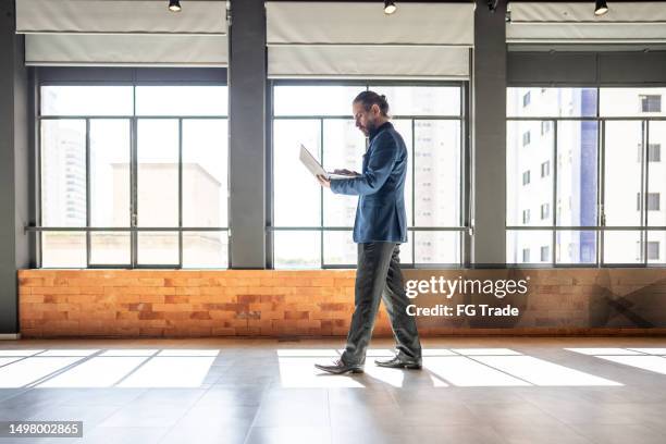 mature businessman walking and using laptop at office - tech founder stock pictures, royalty-free photos & images
