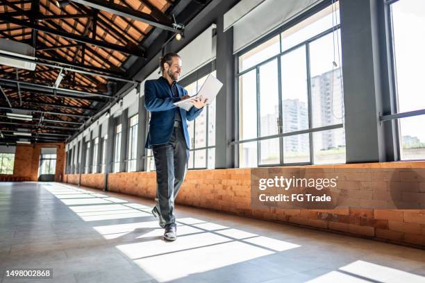 mature businessman walking and using laptop at empty office for sell at real estate - real estate office stockfoto's en -beelden