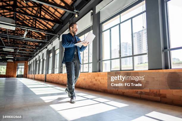 mature businessman walking and using laptop at empty office for sell at real estate - kommersiell egendom bildbanksfoton och bilder