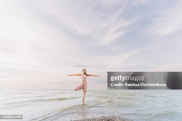 a young adult woman of 40 years old, practicing yoga on the seashore. beautiful sunset and sky - woman stretching sunset bildbanksfoton och bilder
