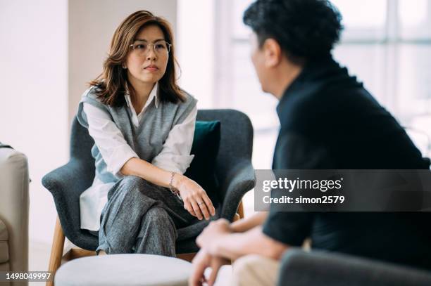navigating challenges: a therapeutic dialogue between an asian female psychologist and a mature man - consulting patient at modern office - difficult conversation stock pictures, royalty-free photos & images