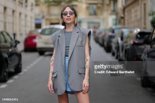 Emy Venturini wears black butterfly sunglasses, gold large earrings, a red pearls and silver cross pendant necklace, a pale gray oversized / ripped...