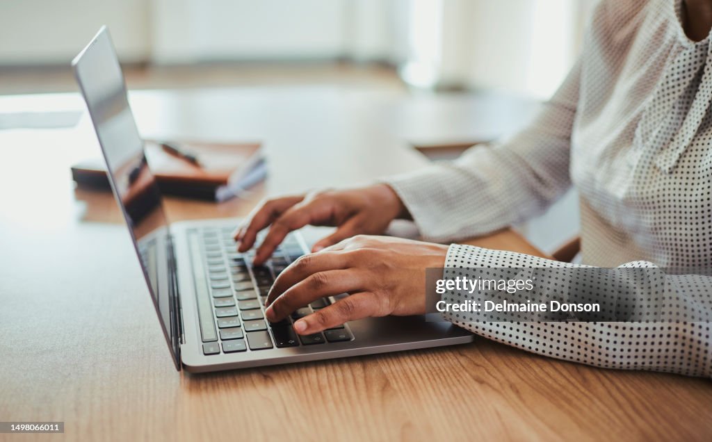 An unrecognized businesswoman sitting at her desk, typing on her laptop computer. Stock photo
