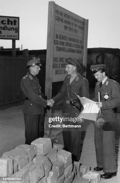 German police officer from the Soviet sector and his counterpart from the Western sector shake hands at the border between the US and Soviet sectors...