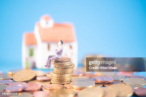 a person sits on a pile of coins. in the background a house. mortage concept. - erfenis stockfoto's en -beelden