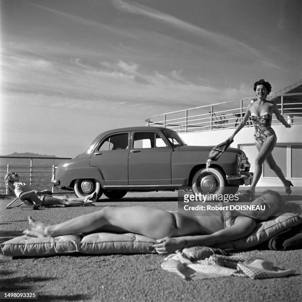 Jeune femme en maillot de bain allongée sur un matelas pneumatique pendant qu'une autre court et une troisième prend un bain de soleil sur une chaise...