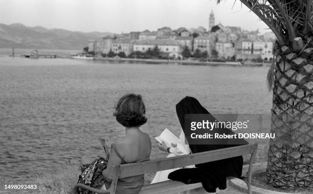Une femme dos nue assise à côté d'une religieuse sur un banc face à la mer à Korcula en Croatie durant l'été 1965.