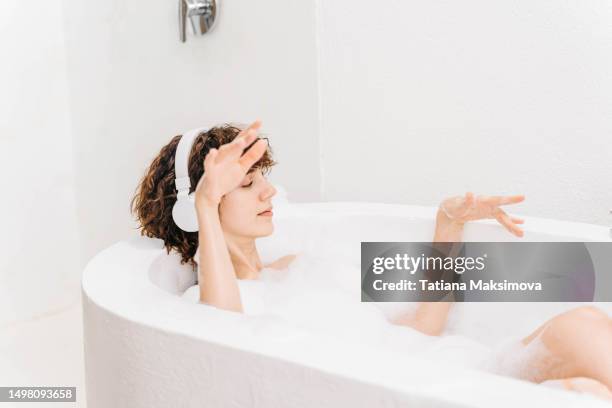 young beautiful woman in white headphones is taking a bath and relaxing. - woman bath bubbles stock-fotos und bilder