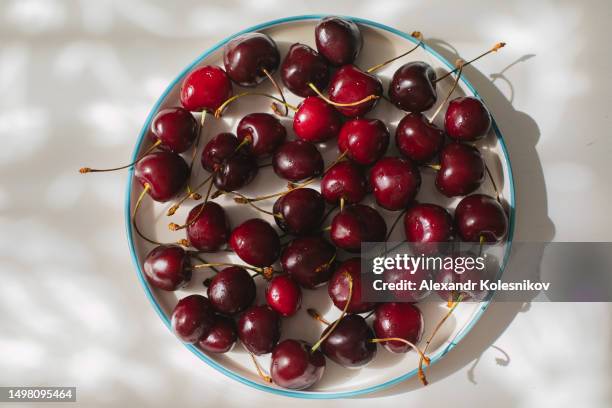 plate of fresh cherry on white kitchen table with shadow sunlight - cherry stock pictures, royalty-free photos & images