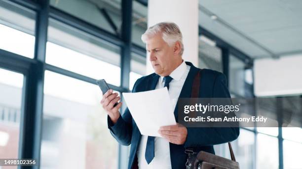 phone, businessman and paper for finance report, reading email or legal contract while walking in office corridor. senior male, corporate worker or travel networking with contact on mobile smartphone - male likeness stock pictures, royalty-free photos & images