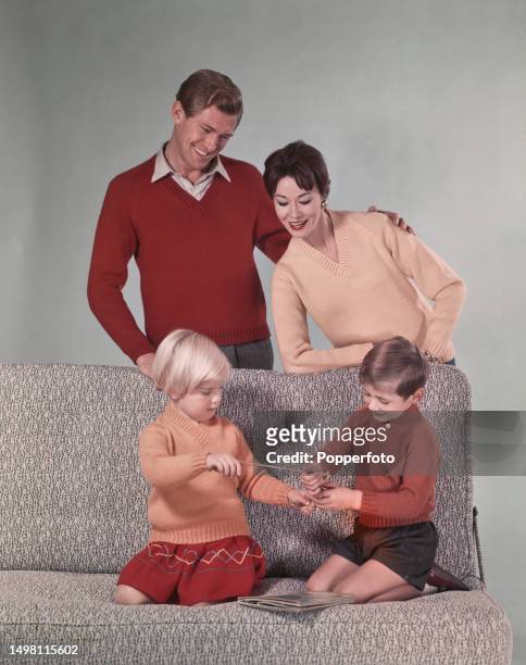 Posed studio portrait of a male and female fashion model posed in a family setting with two children, they all wear matching V-neck sweaters in red...