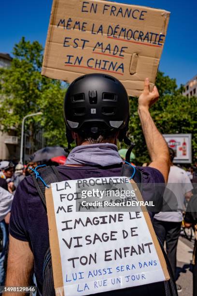 Un manifestant casqué porte une pancarte "EN FRANCE MEME LA DEMOCRATIE EST MADE IN CHINA" et "LA PROCHAINE FOIS QUE TU MATRAQUES IMAGINE LE VISAGE DE...