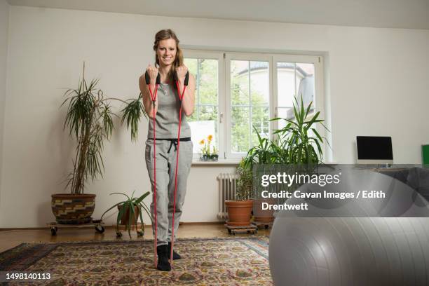 young woman doing exercise with rope in living room, munich, bavaria, germany - exercise room stock pictures, royalty-free photos & images