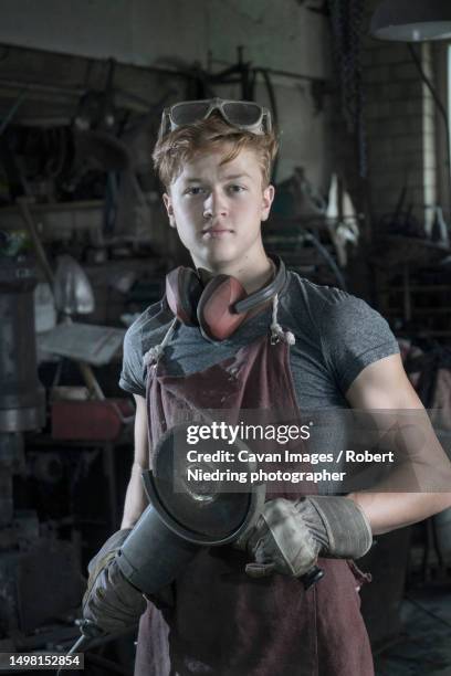 portrait of trainee blacksmith with angle grinder at workshop - metalwork stock-fotos und bilder
