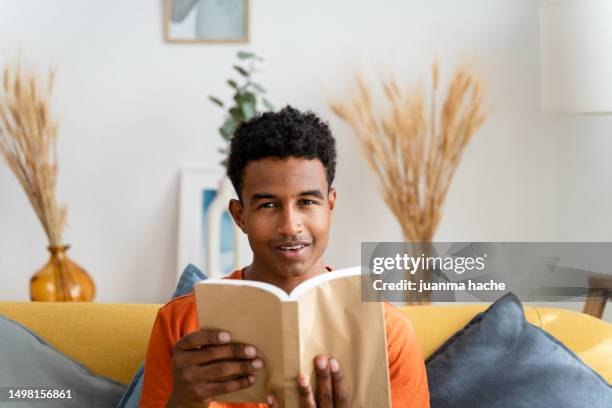 smiling black boy reading book at home - new york city museum of modern art stock-fotos und bilder