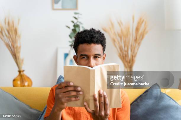 smiling black boy reading book at home - new york city museum of modern art stock-fotos und bilder