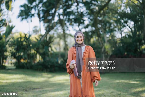asian muslim young woman standing in public park smiling looking at camera with hijab - 長全身裙 個照片及圖片檔