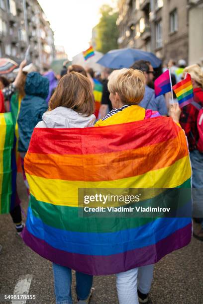 lesbische frauen tragen flaggen während der pride-veranstaltung - regenbogenfahne stock-fotos und bilder
