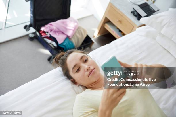 young woman texting on smart phone in hotel room - hotel room white bed stock pictures, royalty-free photos & images