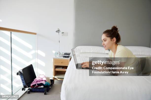 young woman working on laptop in hotel room - hotel room white bed stock pictures, royalty-free photos & images