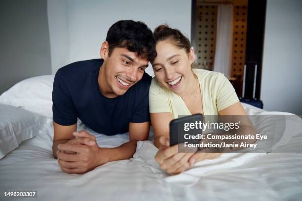 couple using phone in hotel room - hotel room white bed stock pictures, royalty-free photos & images